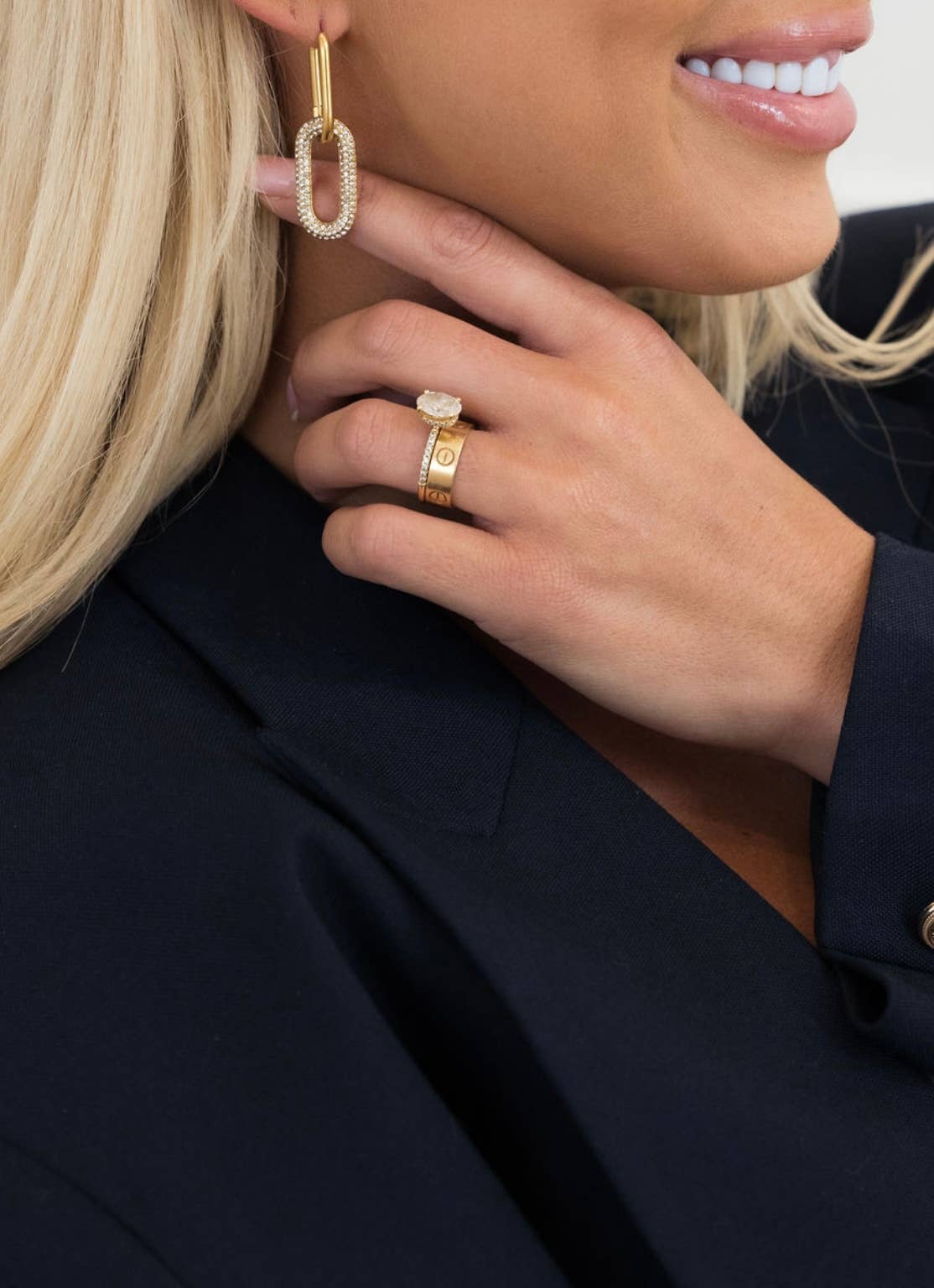 Close-up of a person wearing gold earrings and rings, with a blurred background.