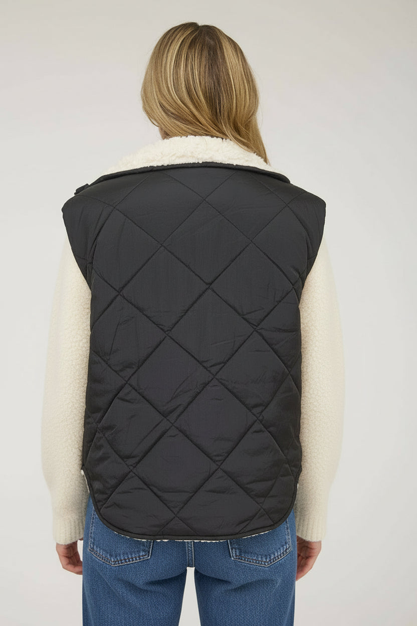 Person wearing a black quilted vest over a striped sweater on a white background