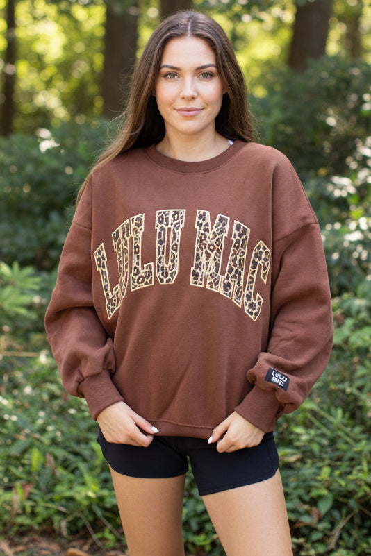 Brown sweatshirt with leopard print text worn by a person on a white background