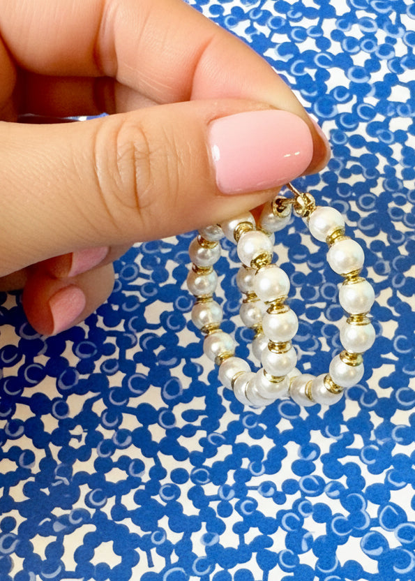 Pearl and gold hoop earrings on a branded card with a blue patterned background