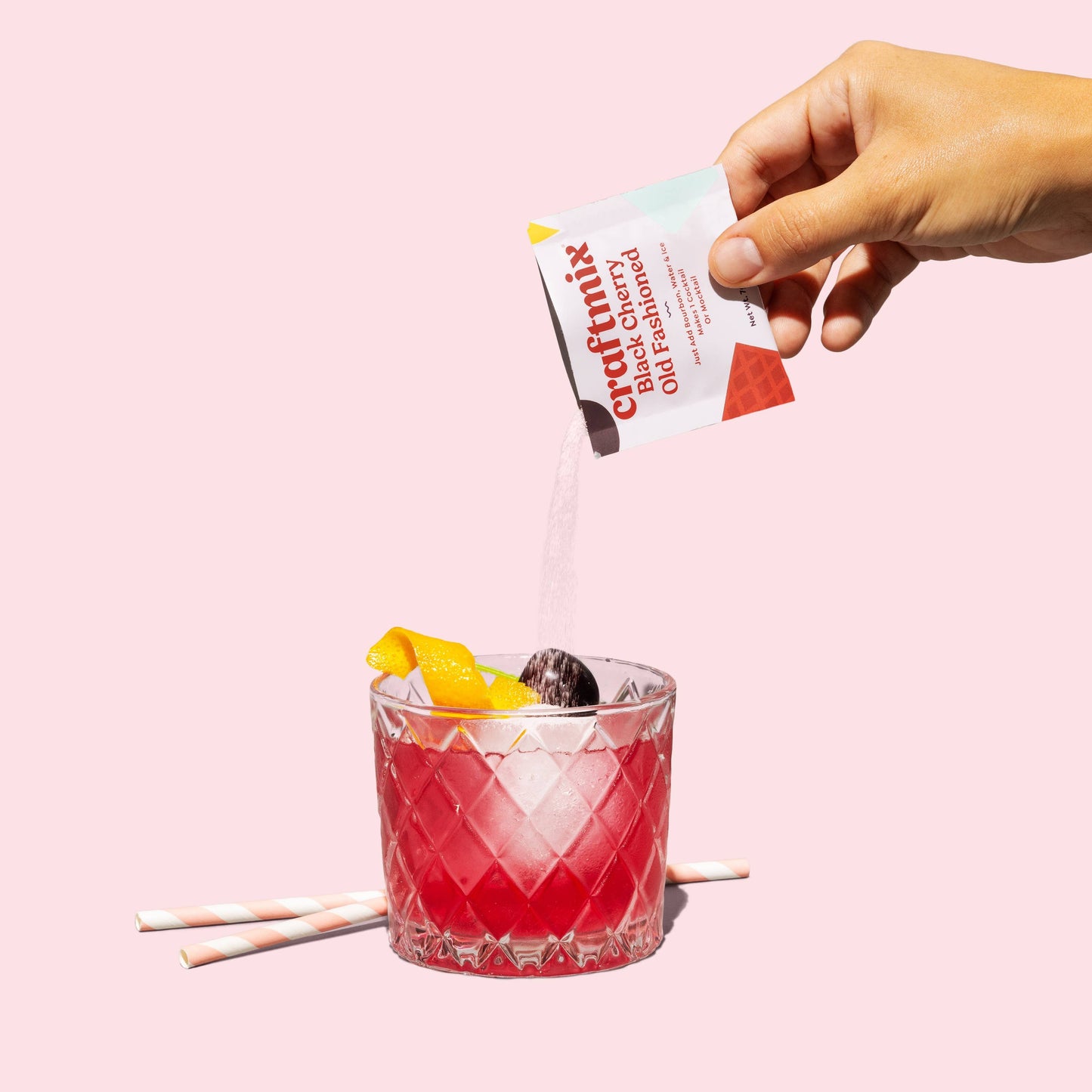 Hand pouring a Crustamix drink mix into a glass with a pink background