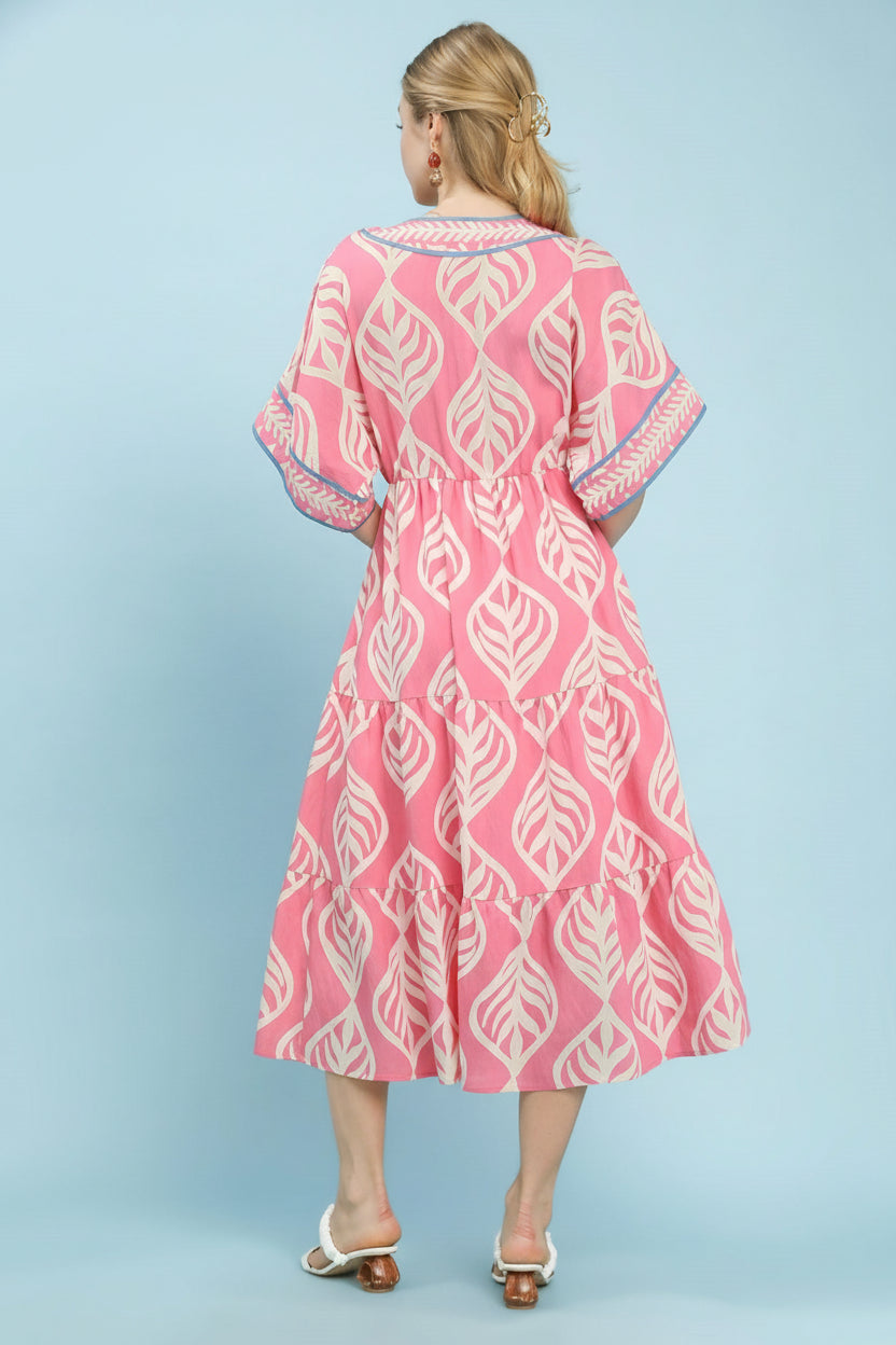 Woman wearing a pink dress with white leaf pattern on a light blue background, featuring Umgee branding.