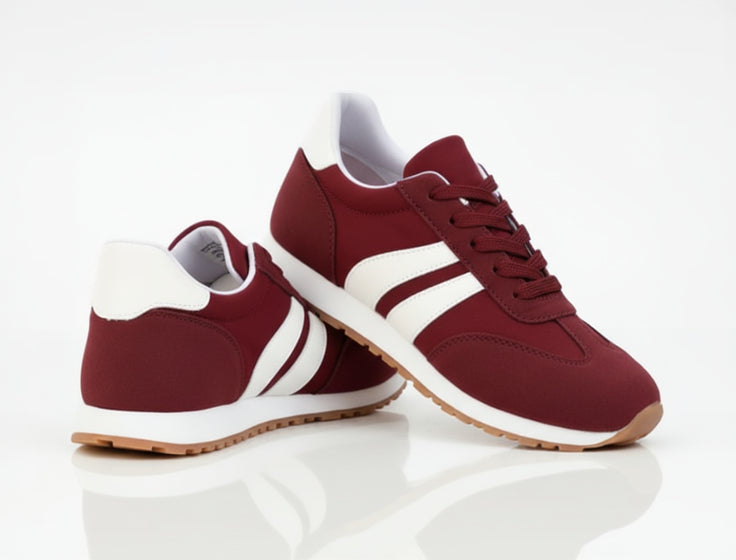 Maroon sneakers with white stripes worn with light blue jeans on a road surface.