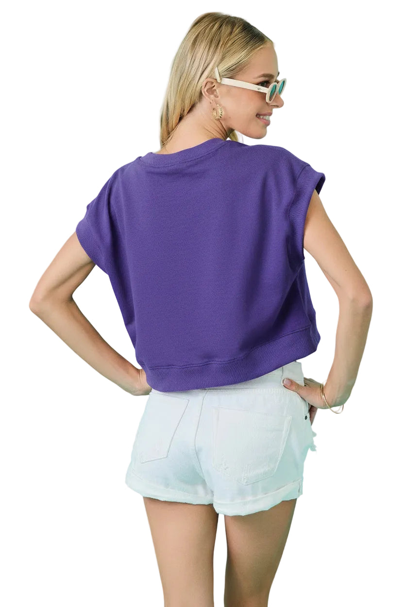 A woman wearing a dark pinkish-red cropped short-sleeve t-shirt and white denim shorts, photographed from the back against a solid turquoise background.
