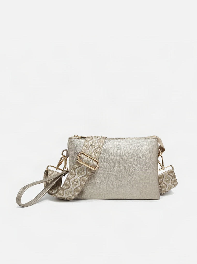 A gold-colored vegan leather crossbody bag with a patterned adjustable strap and two main compartments, displayed against a white background.