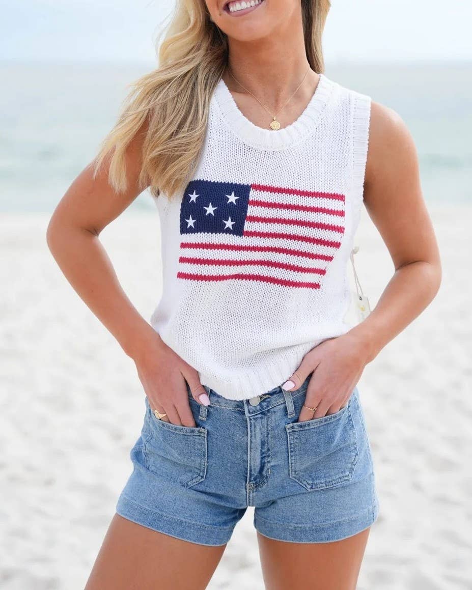 Woman wearing a white sleeveless top with an American flag design on a beach.