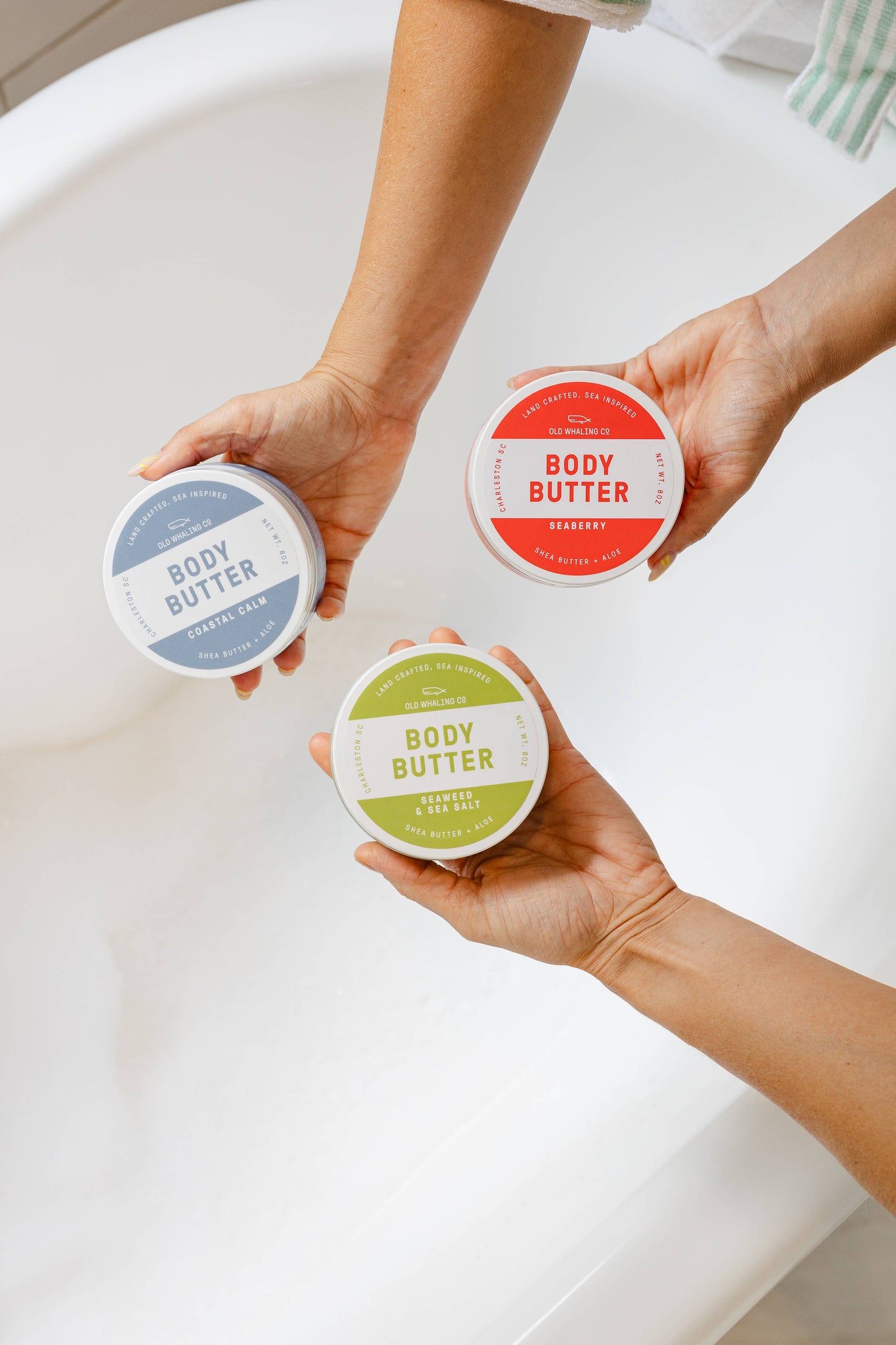 Three containers of body butter held by a person against a white background