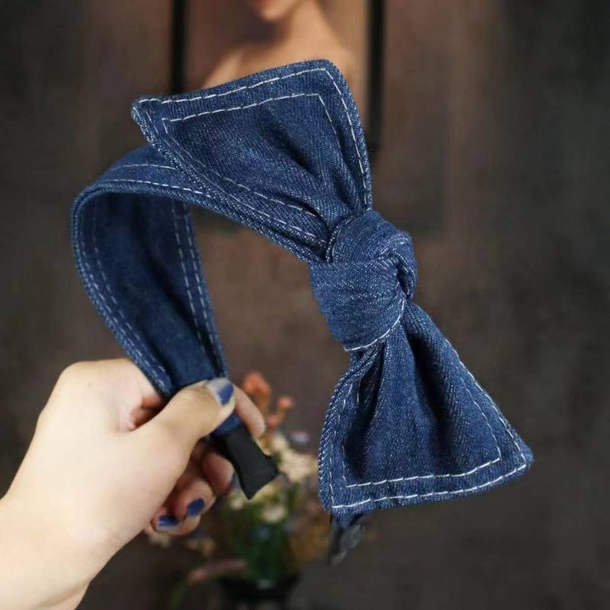 Blue denim bow headband held by a hand against a blurred background