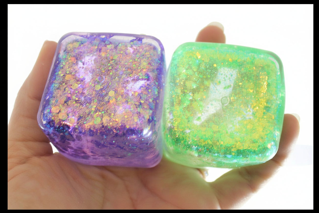 Two glittery square objects, one purple and one green, held in a hand with 'Curious Minds' branding.