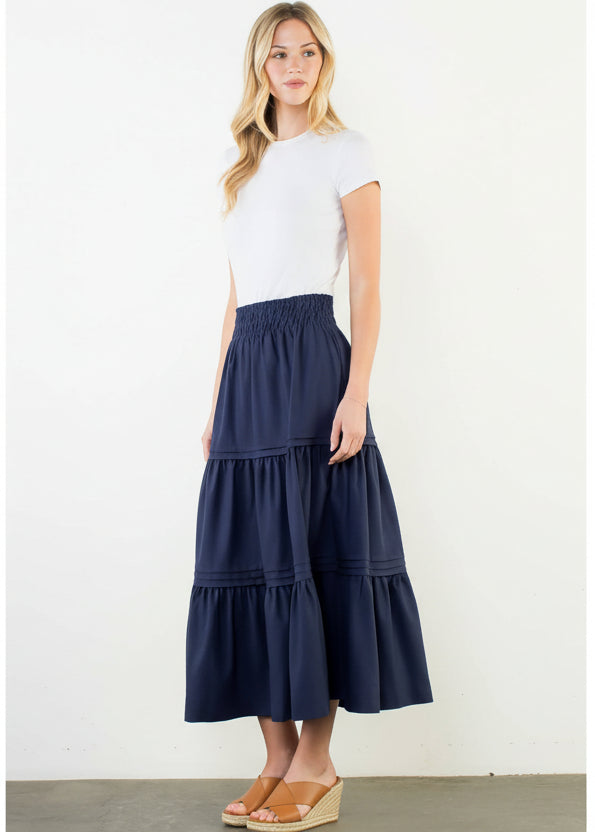 Woman wearing a navy tiered skirt and white top on a white background