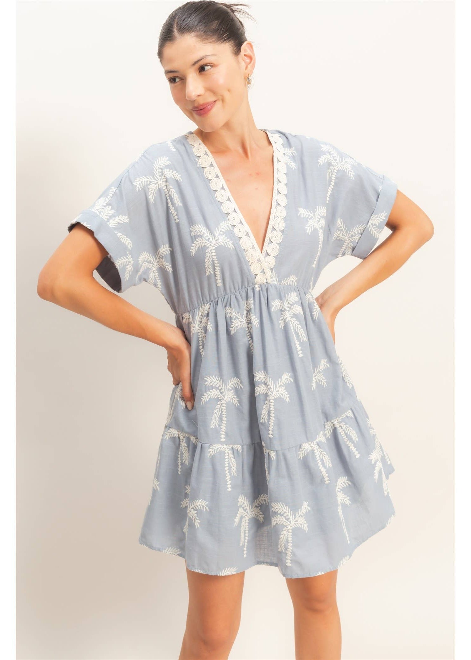 Woman wearing a light blue dress with palm tree pattern on a plain background