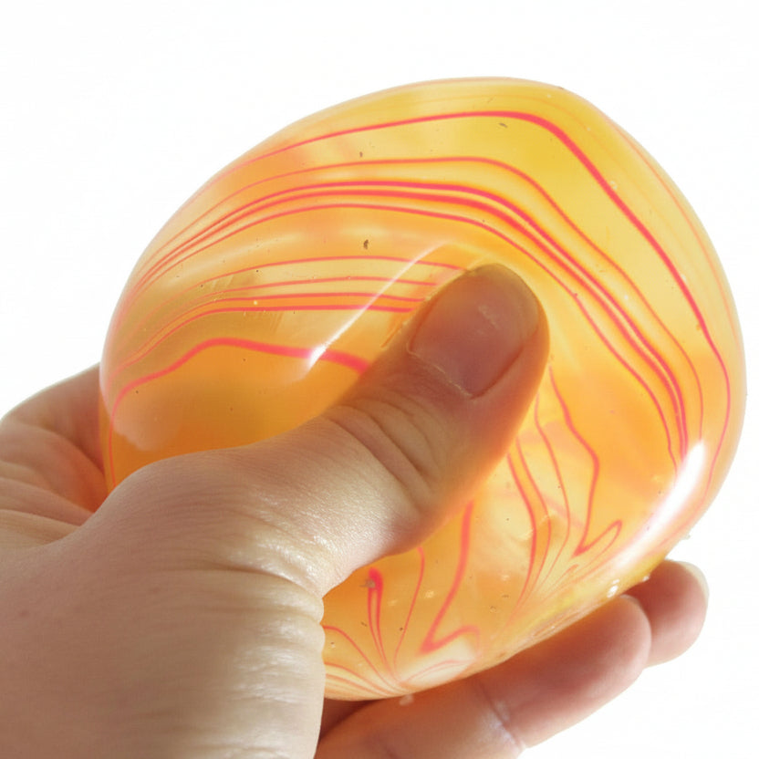 Hand holding a marbled orange and pink stress ball with 'Curious Minds' branding.