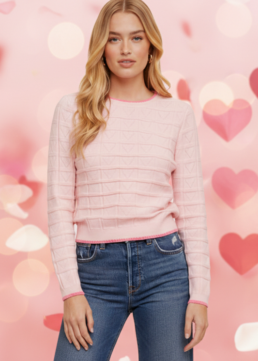 Woman wearing a pink sweater and blue jeans against a heart-patterned background