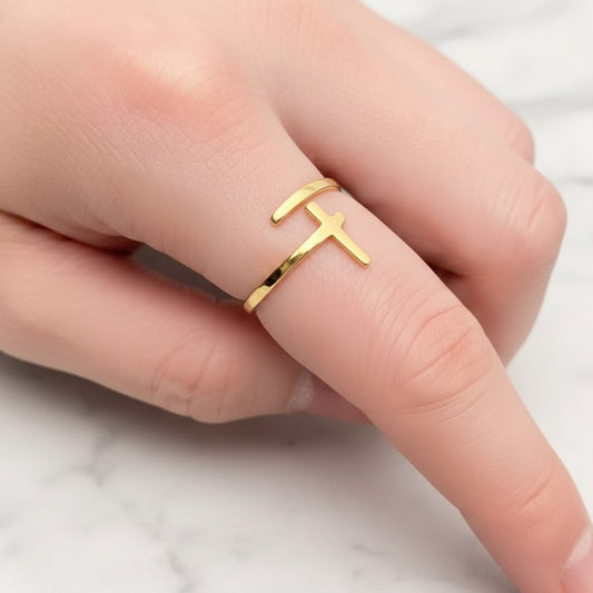 Gold ring with a cross design on a finger against a textured gray background