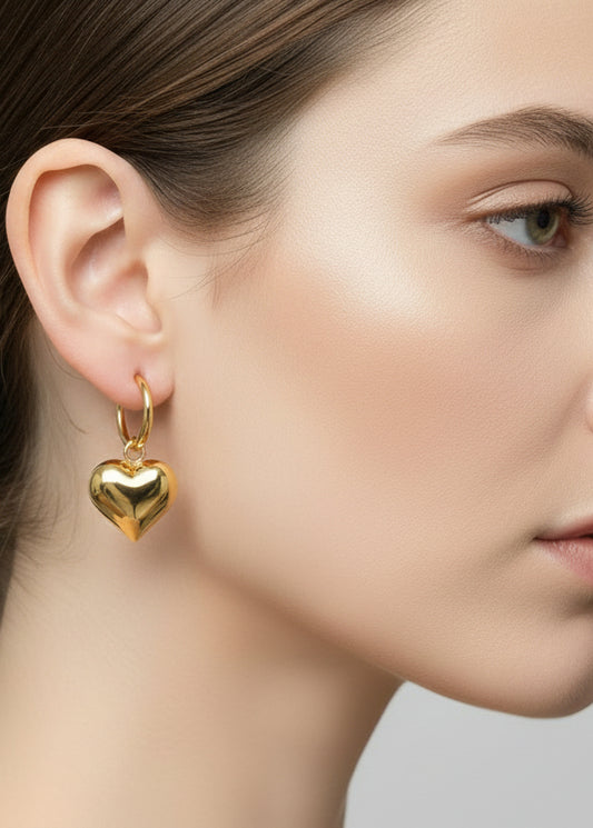 Gold heart-shaped earrings held in a hand against a light background