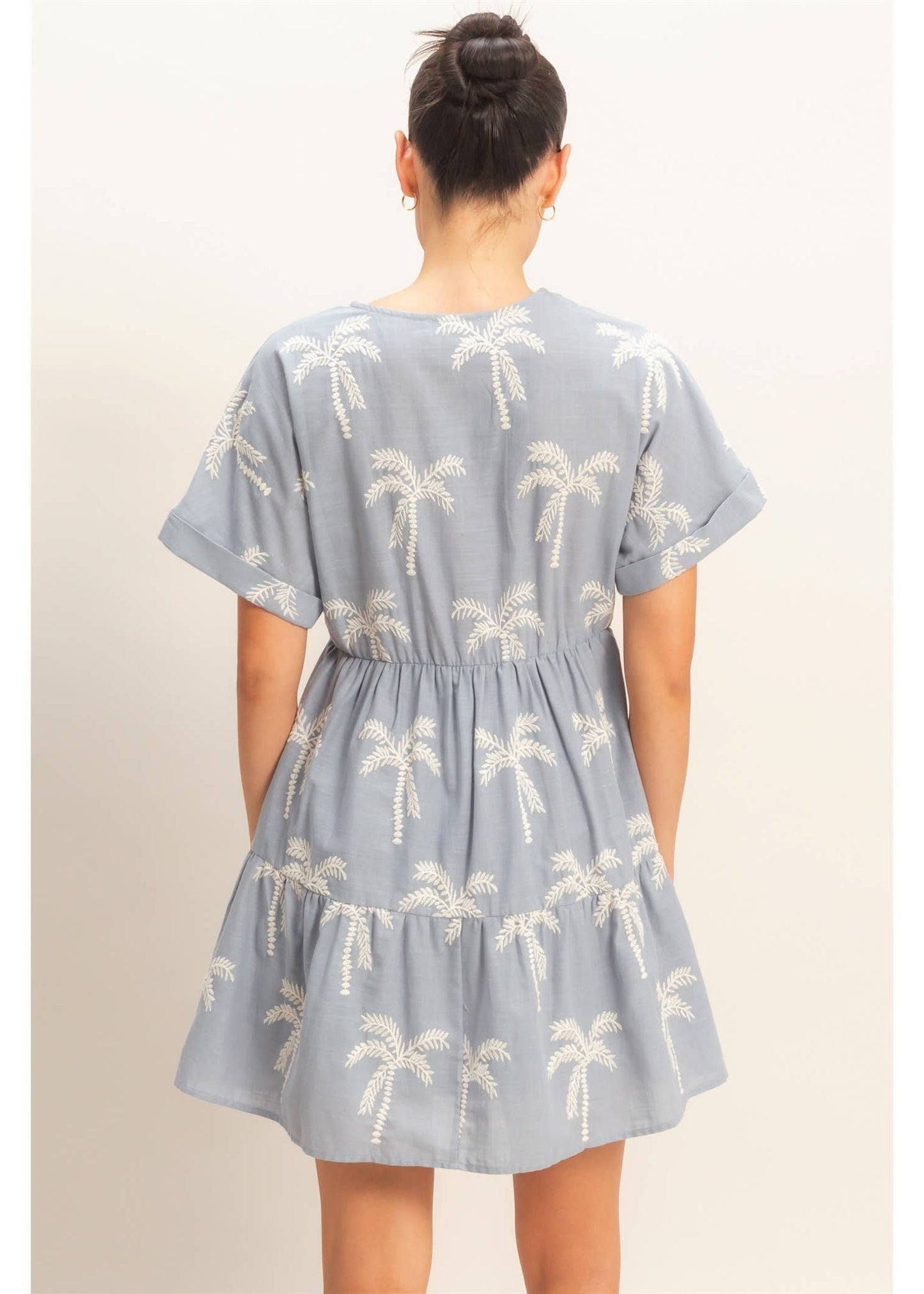 Woman wearing a blue dress with palm tree pattern on a plain background