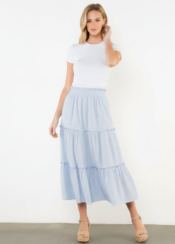 Woman wearing a light blue tiered skirt and white top on a white background