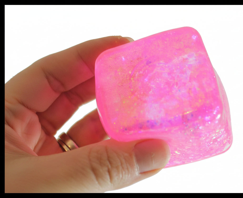 Pink glittery cube held in a hand with 'Curious Minds Busy Bags' logo.