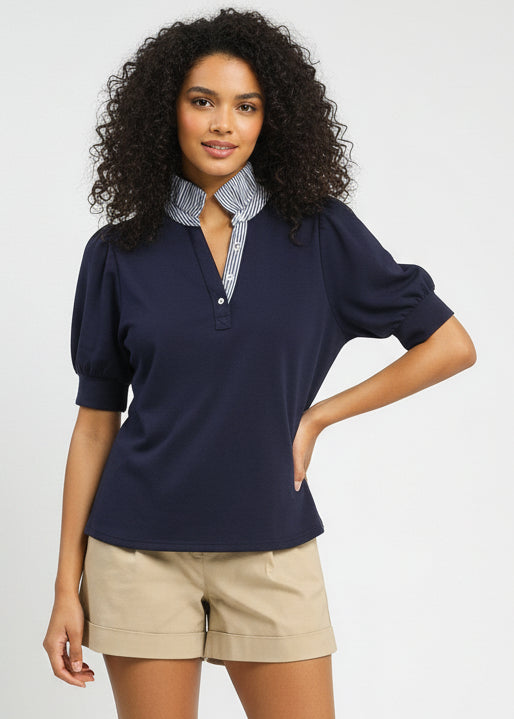 Woman wearing a navy blue sweater with puff sleeves, beige shorts, and brown shoes on a white background.