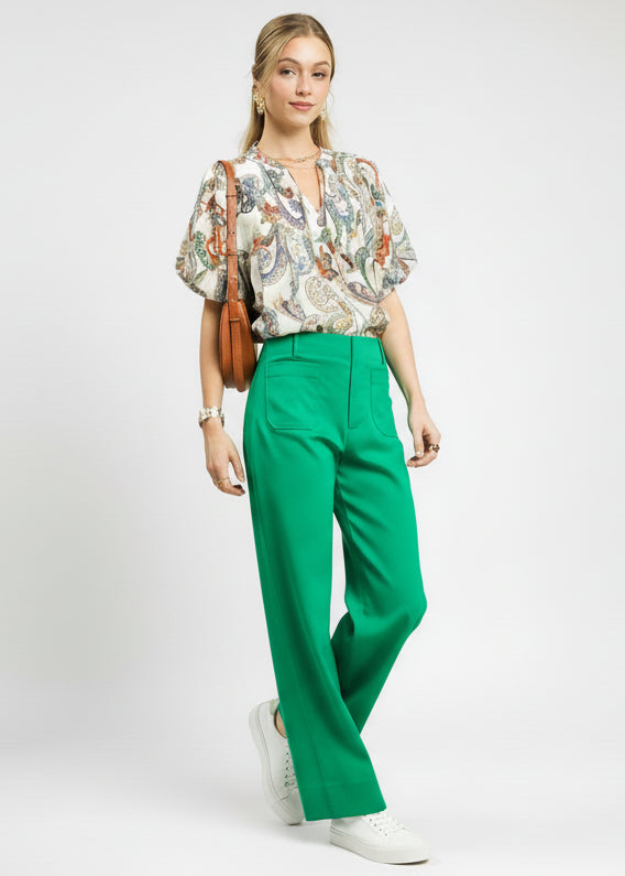 Woman wearing a floral blouse and green pants against a light green background