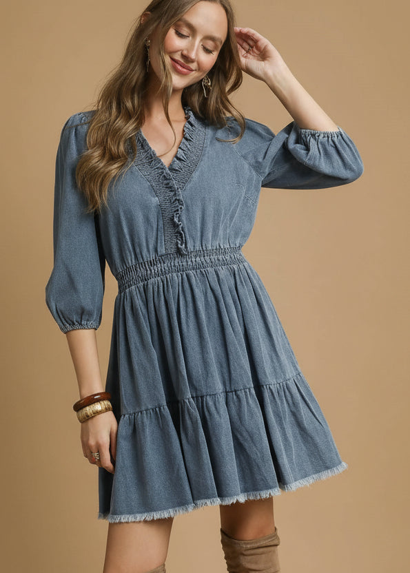 Woman wearing a light denim dress with tiered skirt on a beige background