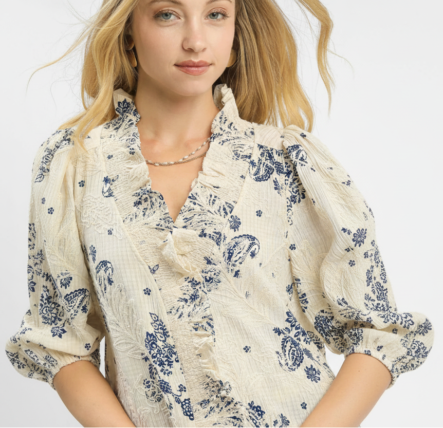 Woman wearing a cream blouse with blue floral patterns on a white background