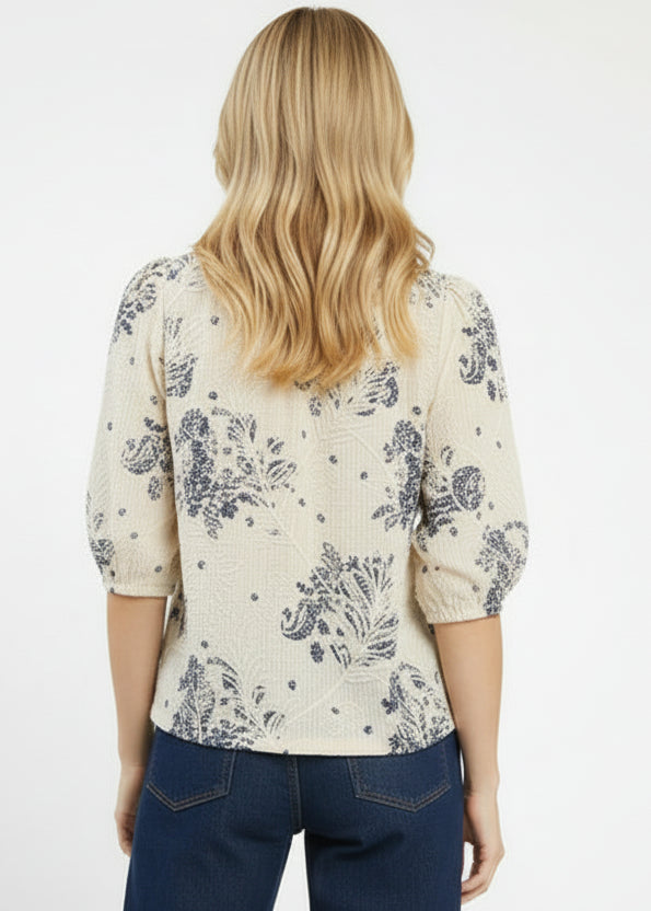 Woman wearing a cream floral blouse with navy blue pants on a white background