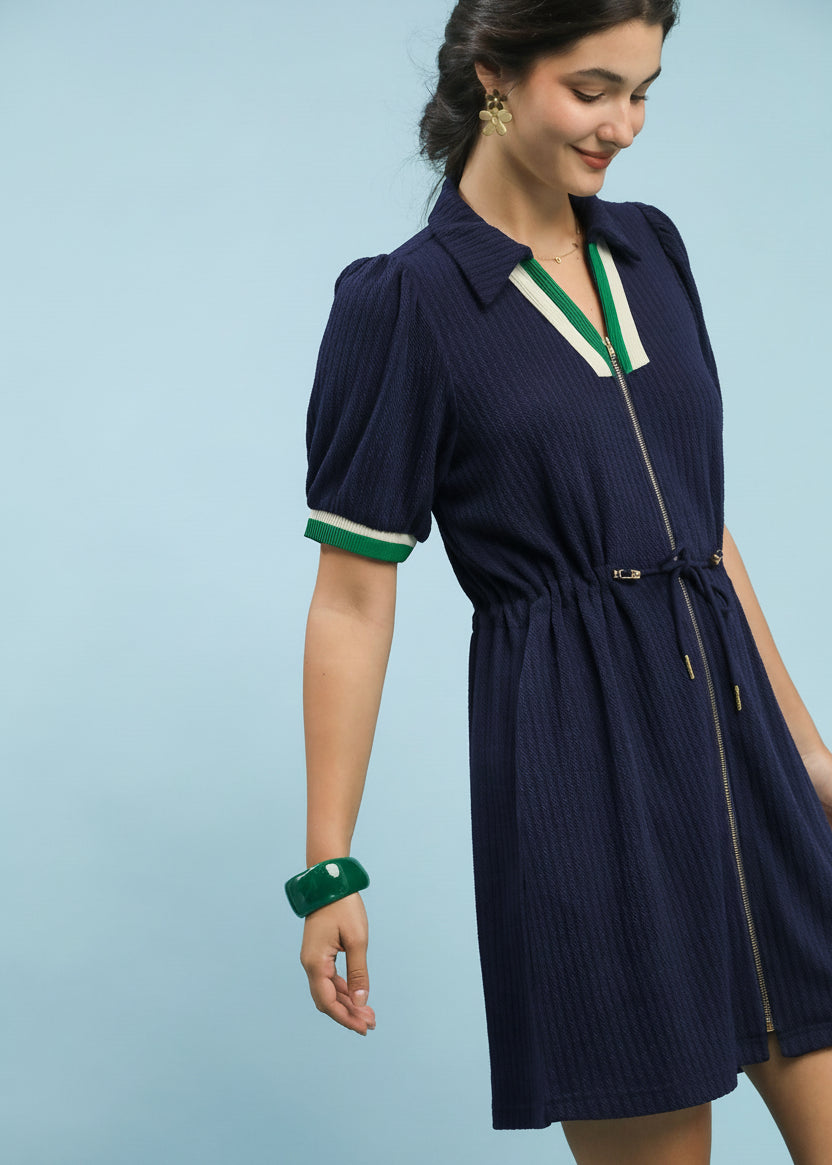 Woman wearing a navy dress with green accents on a light blue background, featuring 'On-The-Go' branding.