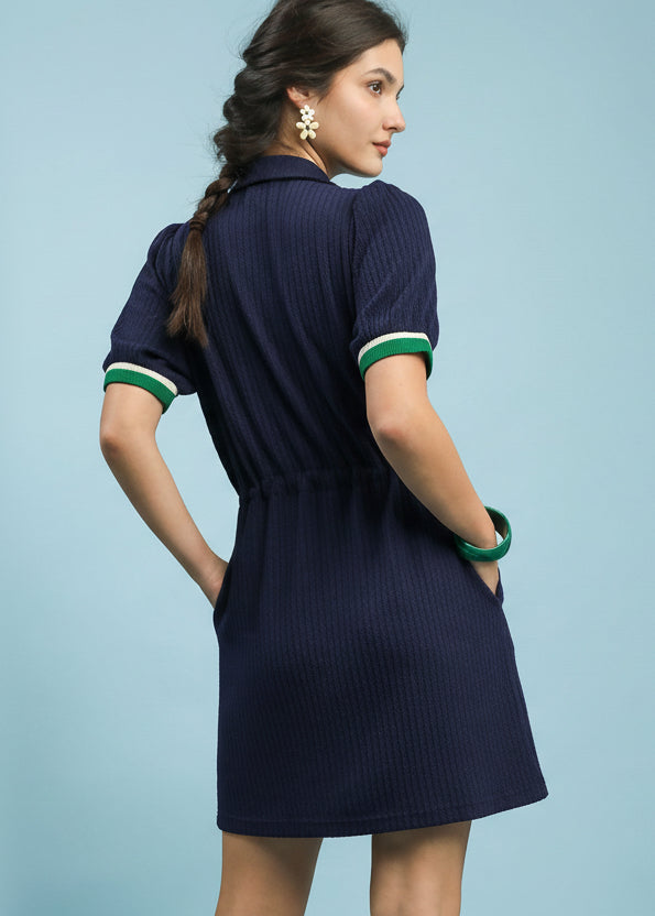 Woman wearing a navy dress with green accents on a light blue background, featuring 'On-The-Go' branding.