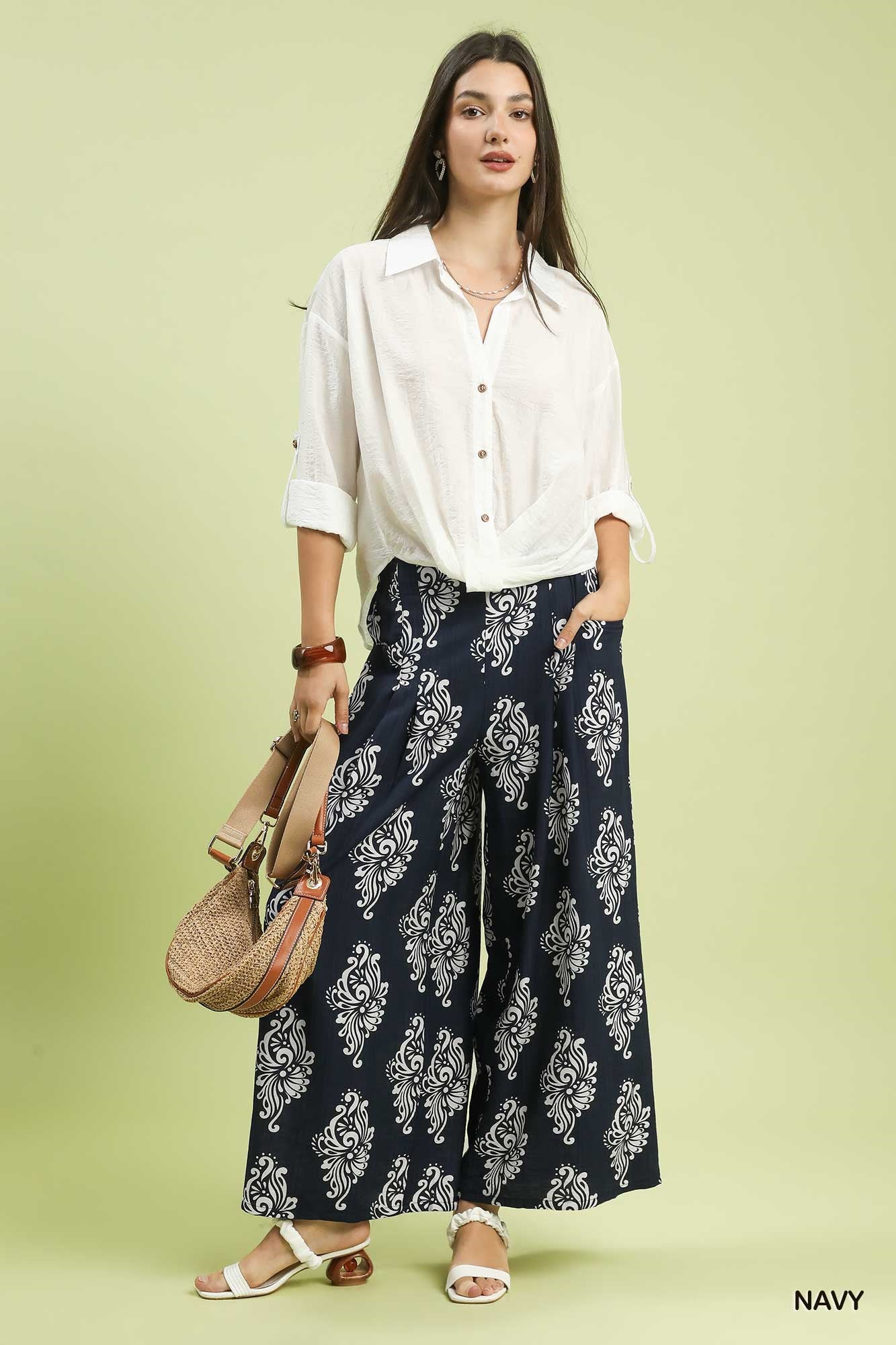 Woman wearing a white shirt and navy patterned pants on a light green background