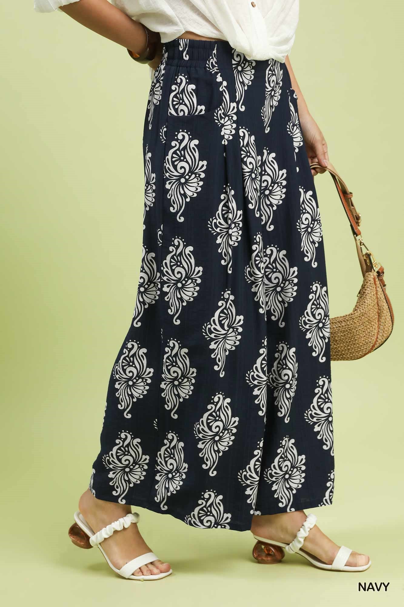 Navy blue wide-leg pants with white floral patterns worn by a person on a light green background.