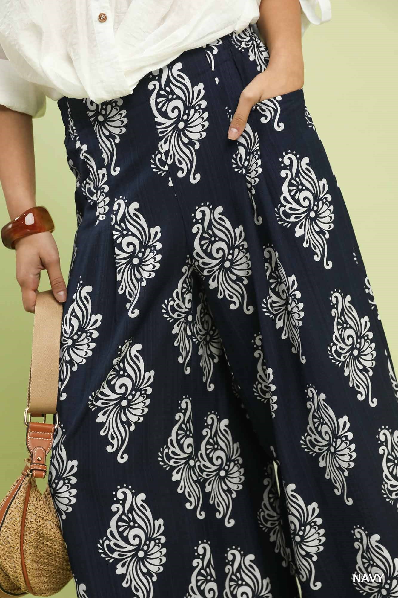 Navy blue pants with white floral patterns worn by a person, against a light green background.