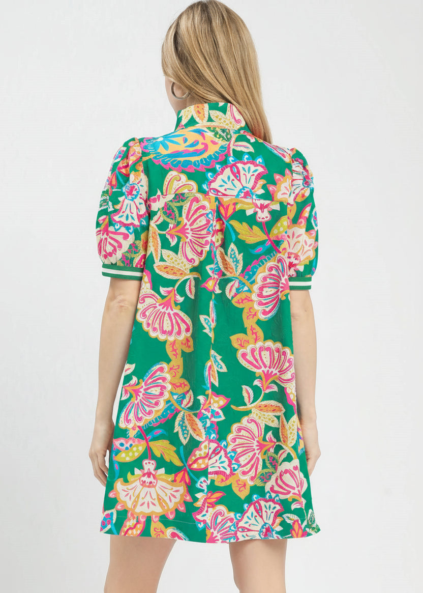 Woman wearing a colorful floral dress with a visible brand logo on a white background