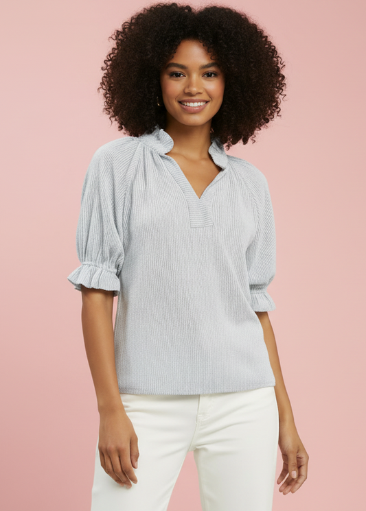 Woman wearing a light blue striped blouse with ruffled sleeves against a pink background
