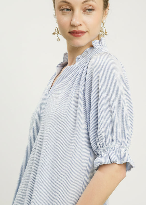Woman wearing a light blue and white striped blouse against a green background