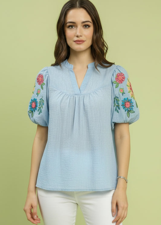 Woman wearing a blue blouse with floral embroidery on a green background