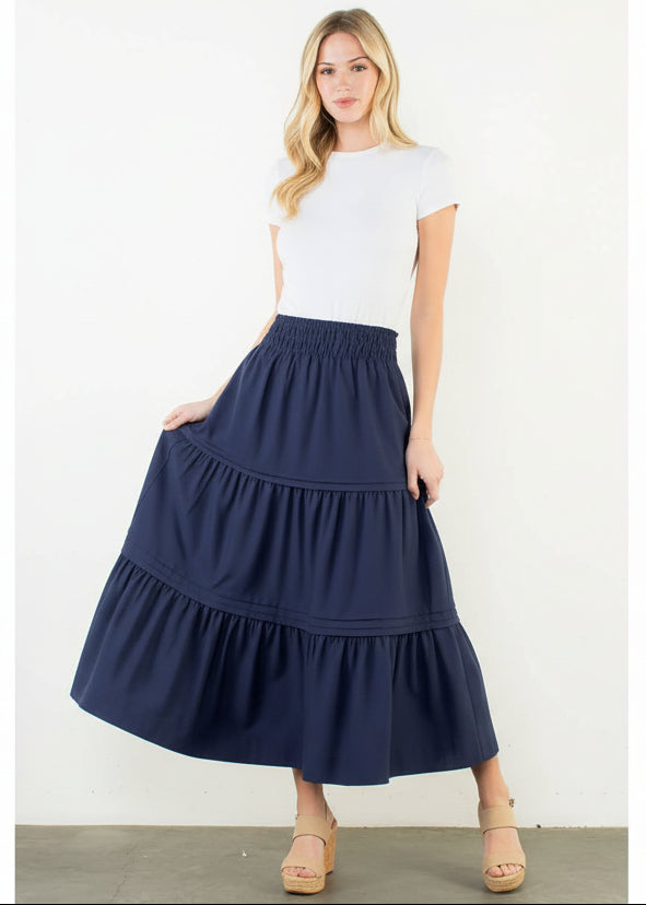 Woman wearing a navy blue tiered skirt and white top on a white background