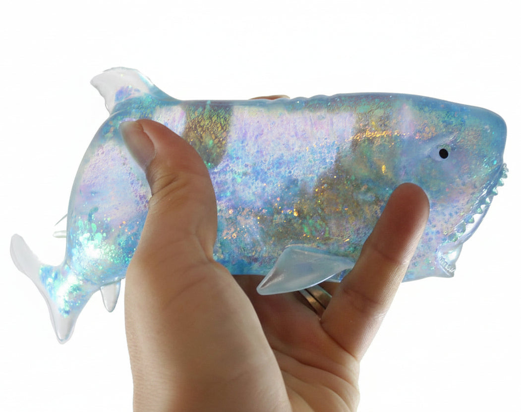 Hand holding a colorful, iridescent fish-shaped object with 'Curious Minds' branding.