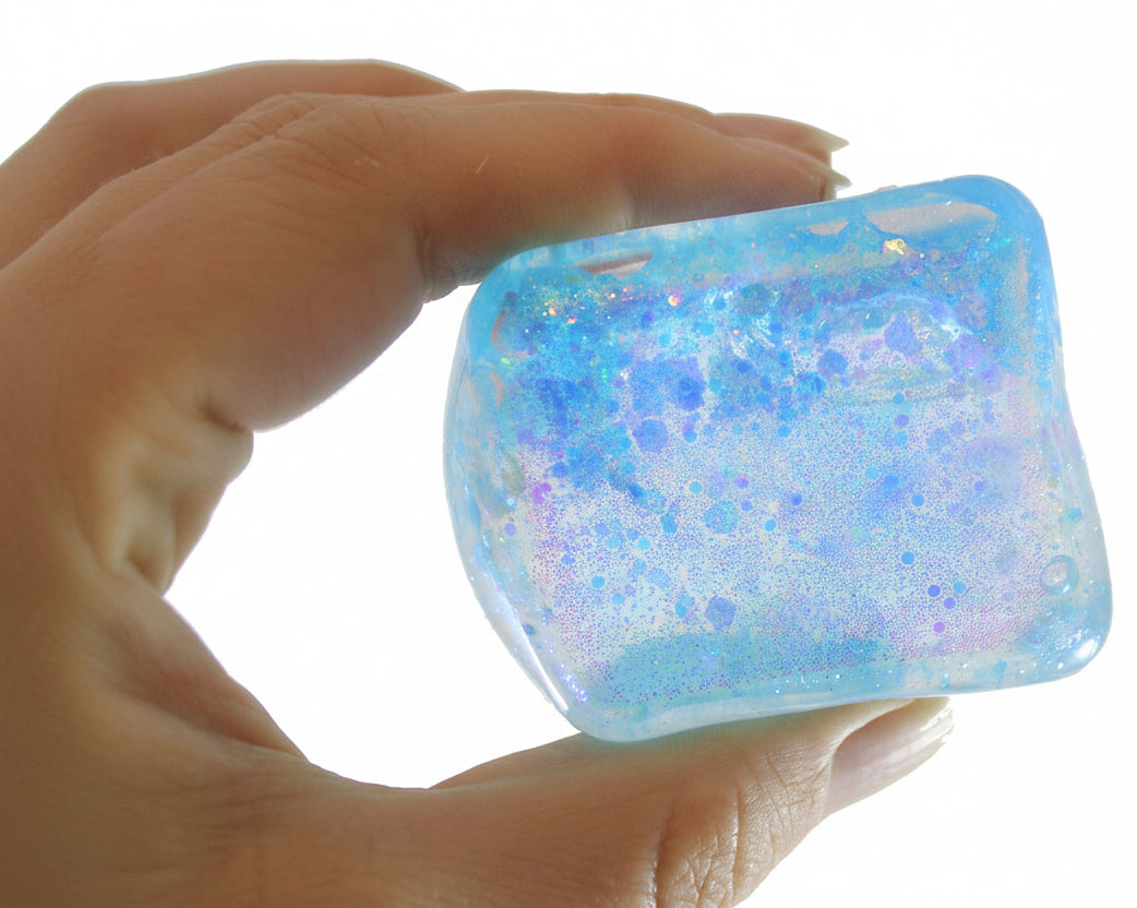 Hand holding a glittery blue and white cube with 'Curious Minds Busy Bags' logo.