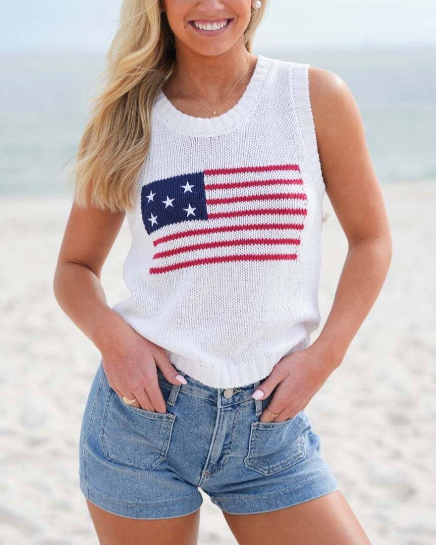 Woman wearing a white sleeveless top with an American flag design on a beach.