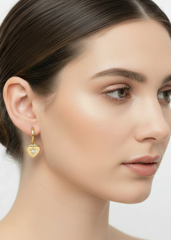 Gold heart-shaped earrings with star designs held in a hand against a white background