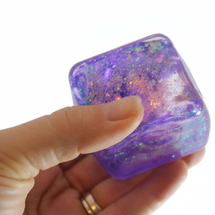 Hand holding a glittery purple and pink cube with 'Curious Minds Busy Bags' branding.