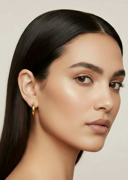 Gold hoop earrings held in a hand against a textured gray background