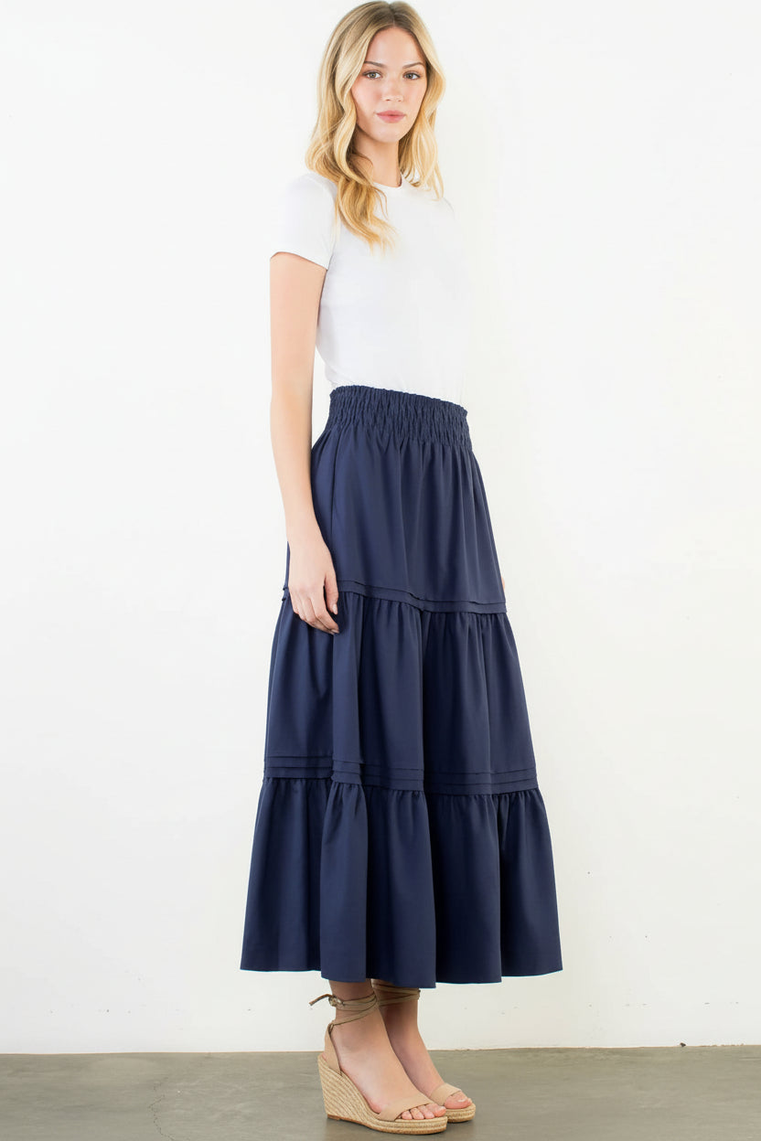 Woman wearing a navy tiered skirt and white top on a white background