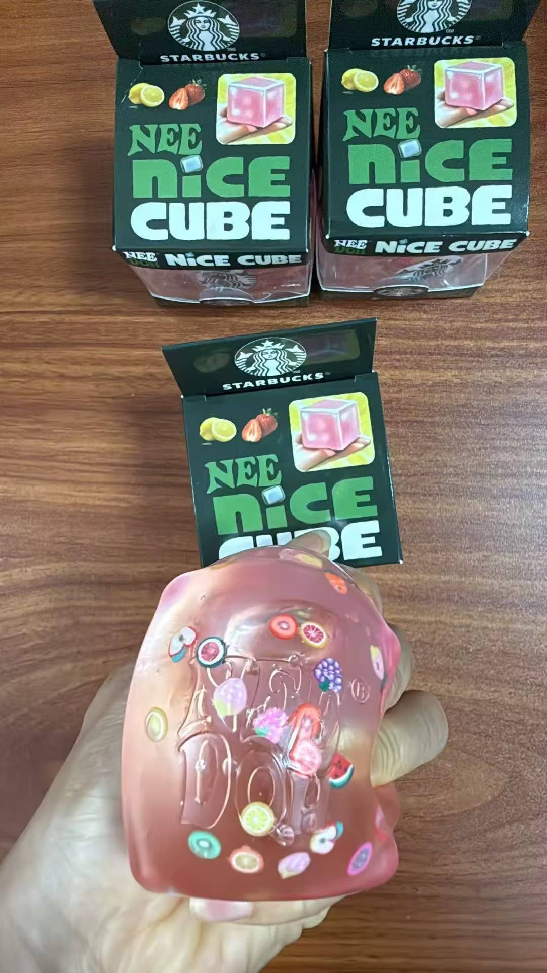 Two boxes of Starbucks Nee Nice Cube on a wooden surface with a hand holding a colorful cube.