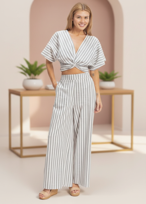 Woman wearing a striped outfit in a minimalistic setting with plants and tables.