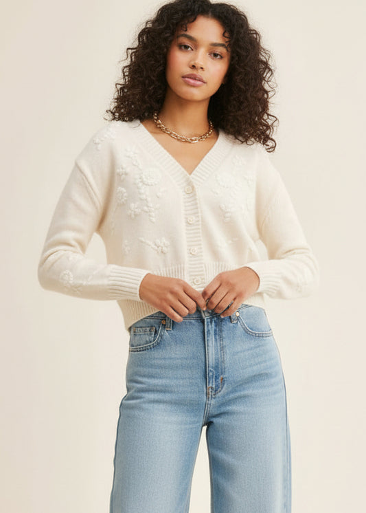 Woman wearing a white cardigan and light blue jeans against a plain background