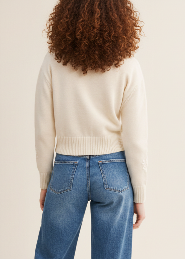 Person wearing a cream sweater and blue jeans on a beige background