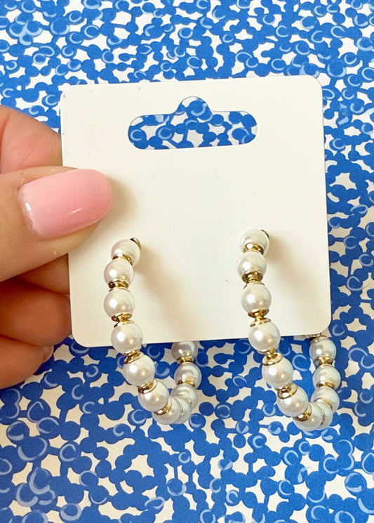Pearl and gold hoop earrings on a Sandy Rizzo branded card against a blue and white patterned background.