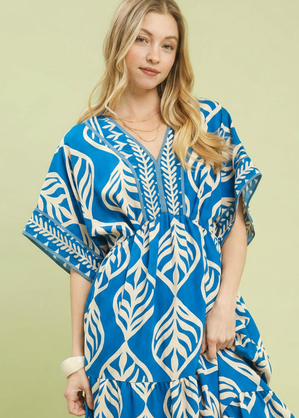Woman wearing a blue and white patterned dress on a light green background with Umgee branding.